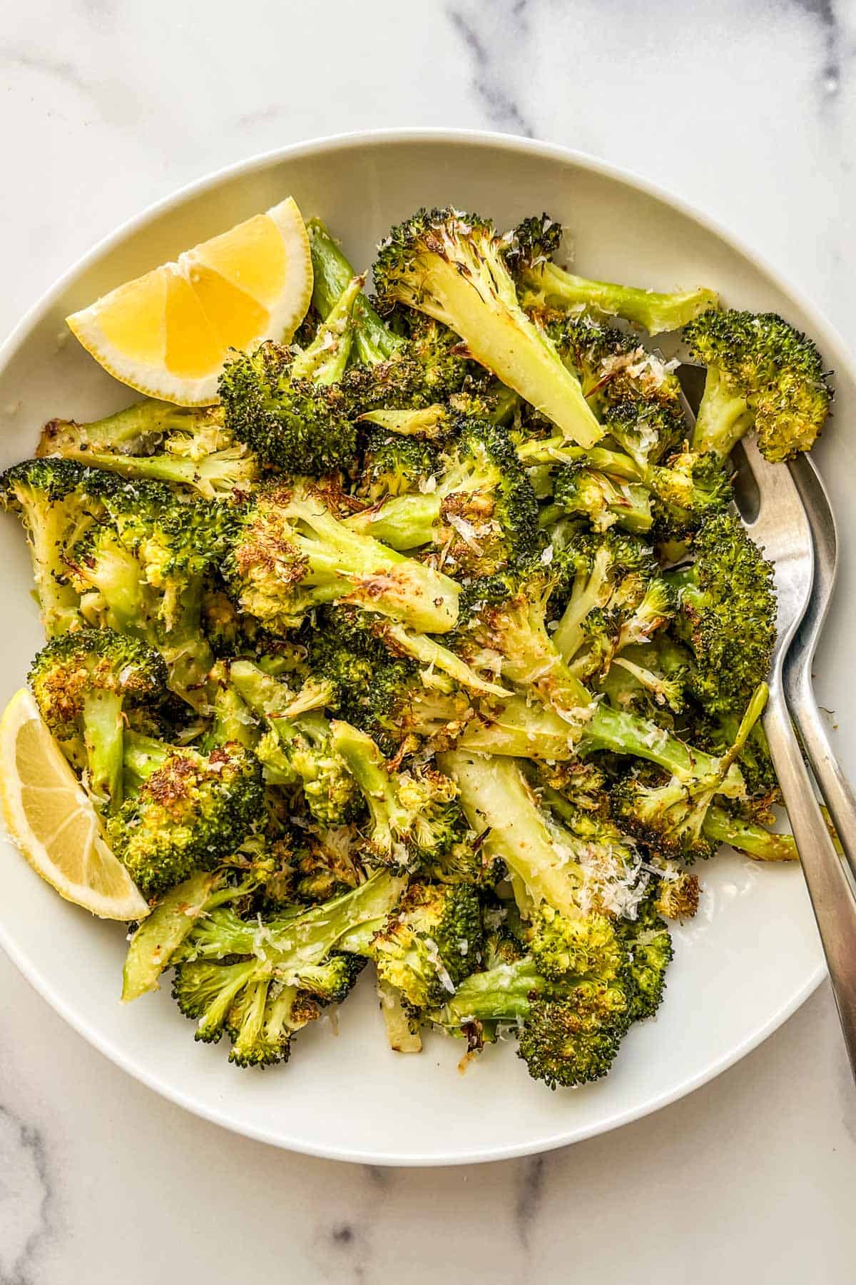 Parmesan roasted broccoli in a white bowl with silver serving utensils.