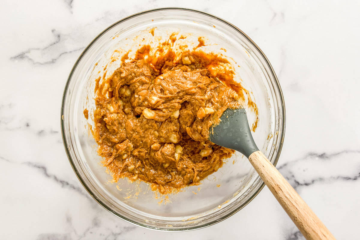 Mashed bananas mixed with coconut sugar and peanut butter in a glass bowl with a spatula.