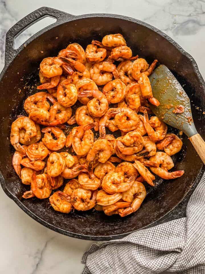 Blackened shrimp in a cast iron skillet with a checked dishcloth.