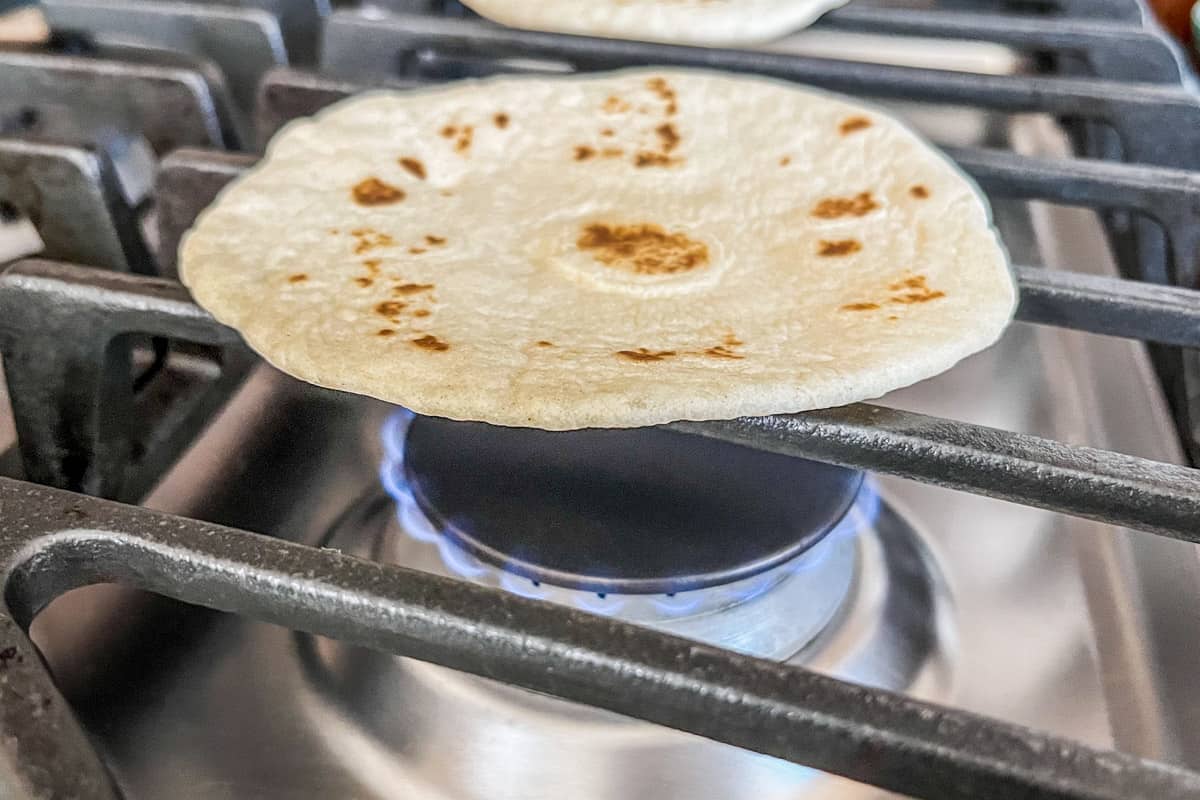 A small tortilla heating on a gas range.