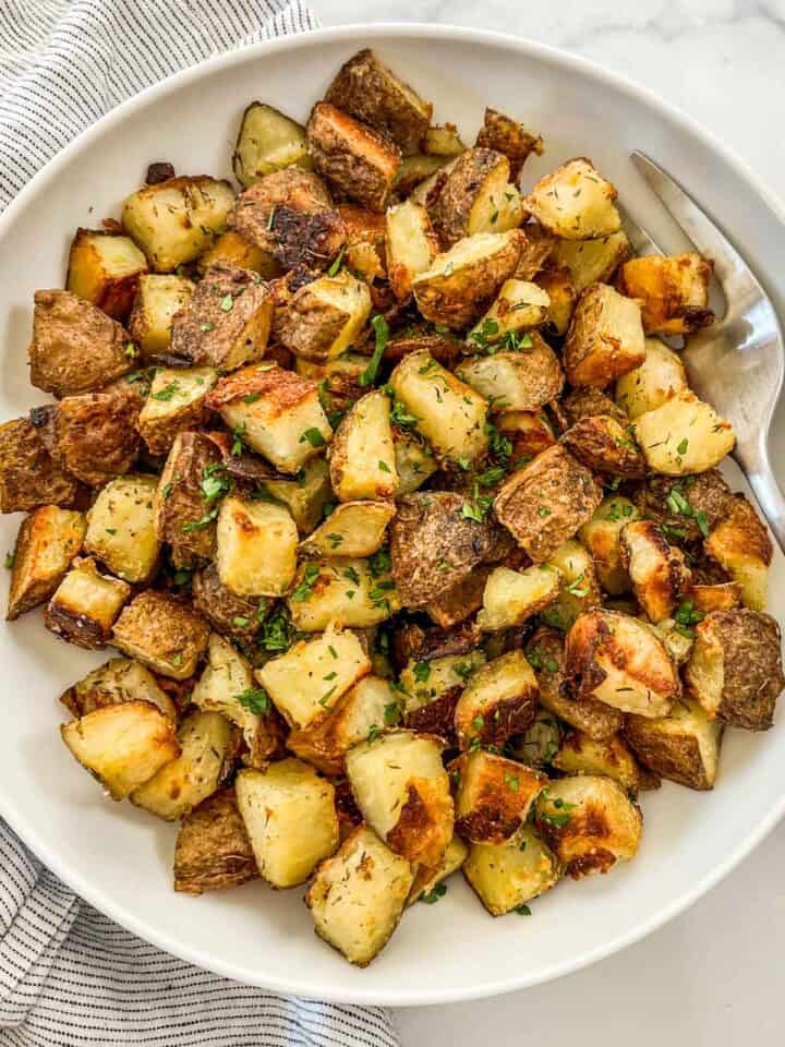 Crispy oven roasted potatoes in a large white serving bowl with a serving fork.