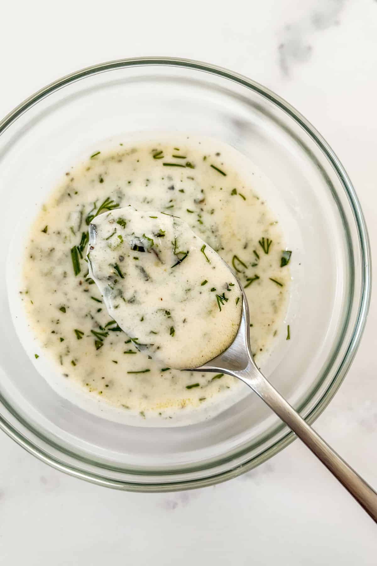 A spoon scooping up yogurt dill dressing from a glass bowl.