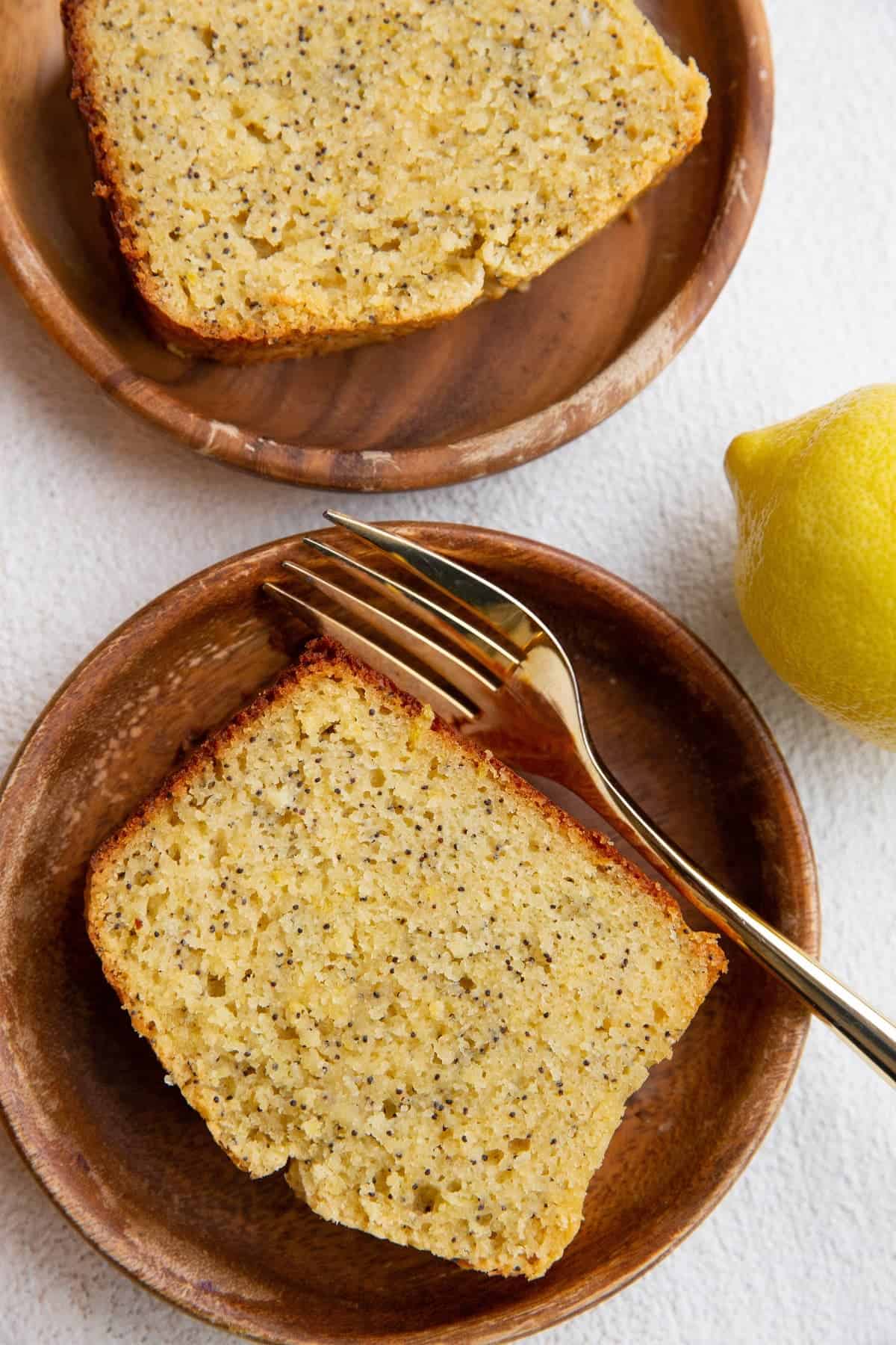 Almond flour lemon poppy seed bread on wooden plates with a gold fork.