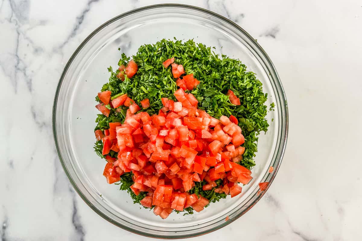 Chopped parsley and tomatoes in a large glass mixing bowl.
