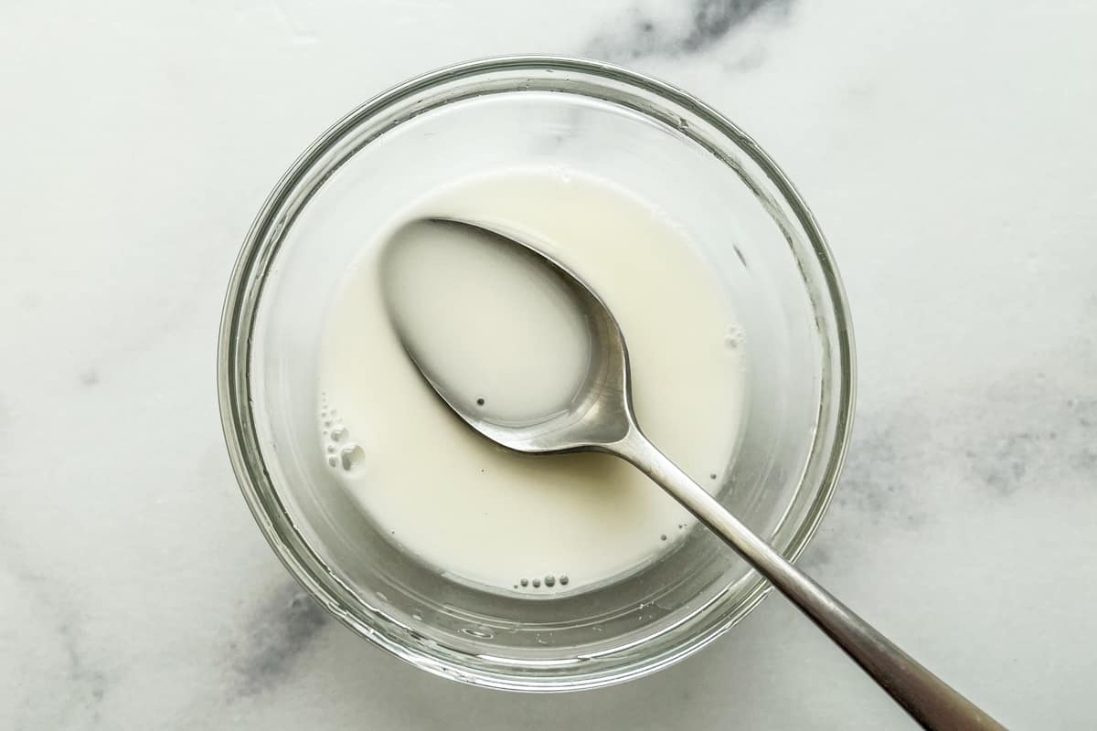 Corn starch and water mixed in a small glass bowl with a silver spoon.