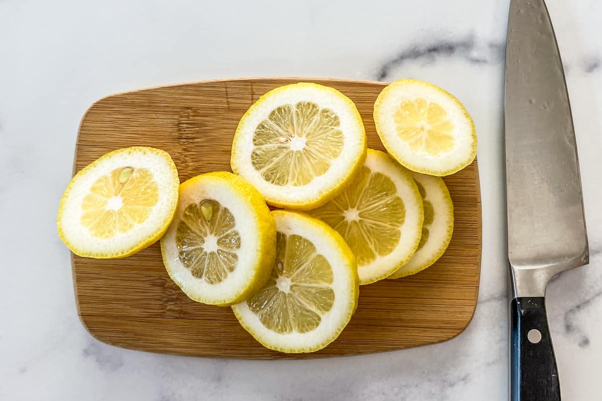 Sliced lemons on a small wooden cutting board next to a knife.