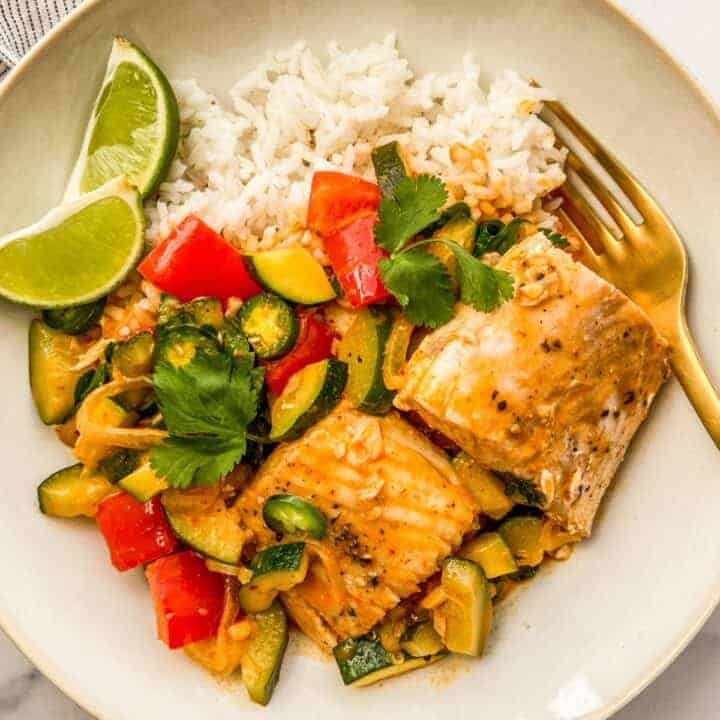 Thai fish curry with white rice and lime wedges in a white bowl.