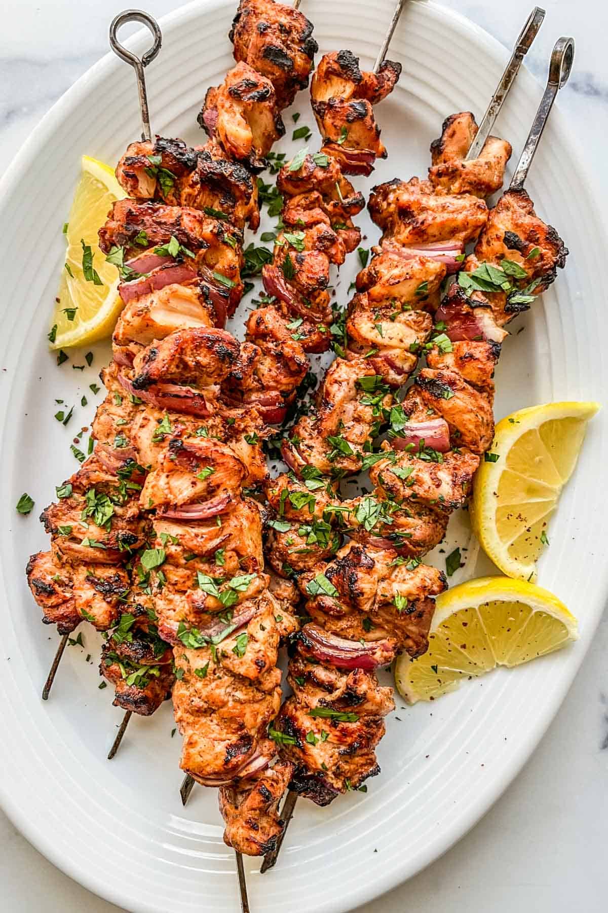 Grilled Turkish chicken kabobs on a white platter with sliced lemons.