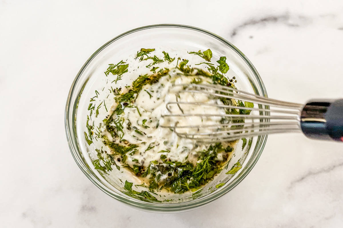 Mixing yogurt dill dressing in a small glass bowl with a small whisk.