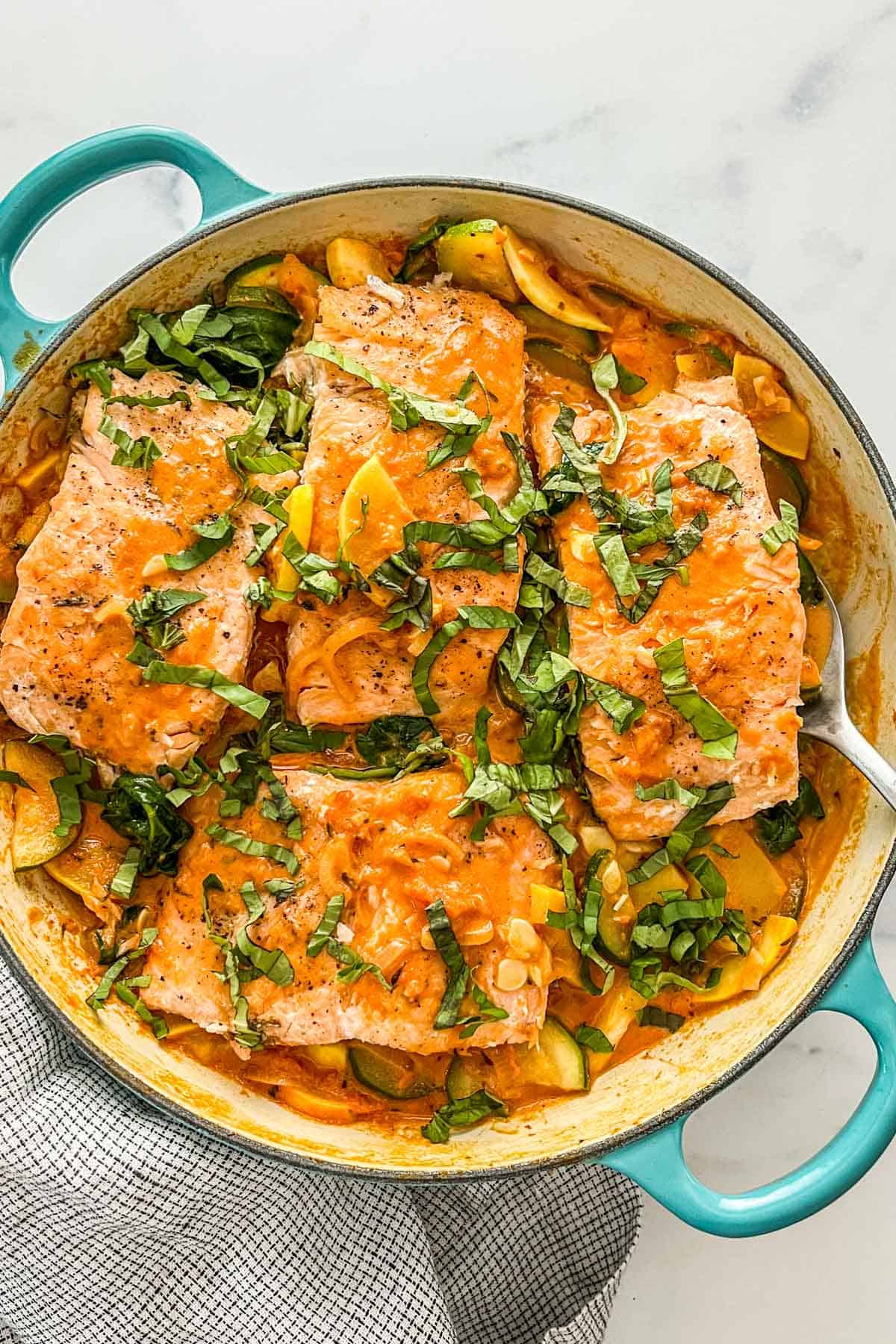 A creamy sauce with salmon and vegetables in a teal skillet.