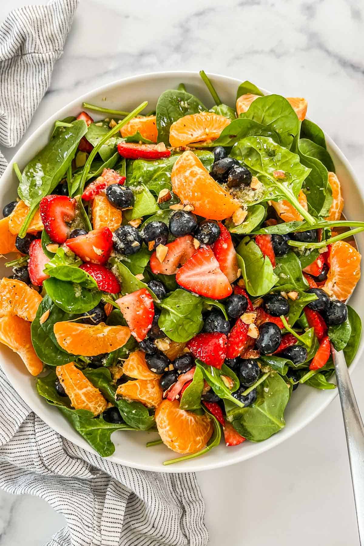 A citrus berry spinach salad in a white bowl with a silver spoon.