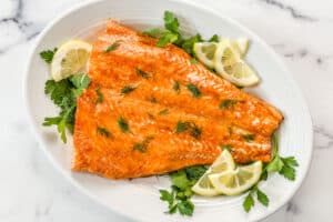 Baked king salmon topped with herbs on a white platter.