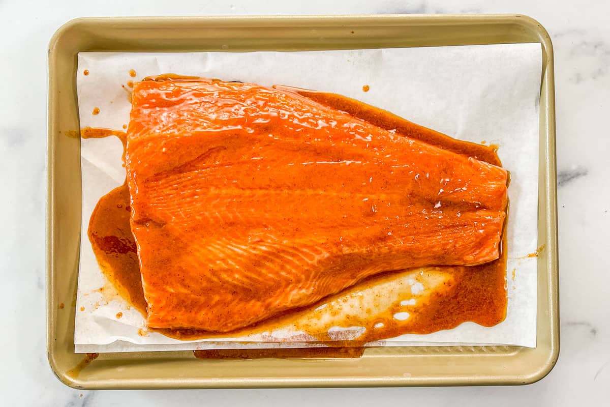 Marinade on top of the king salmon on a parchment lined sheet pan.