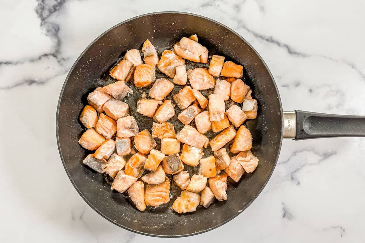 Salmon chunks being cooked in a skillet.
