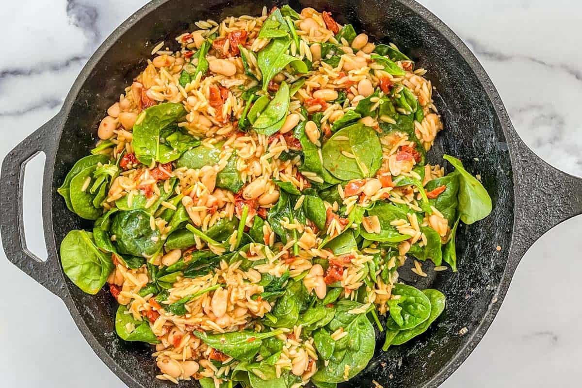 Savory orzo and white beans with spinach in a large cast iron skillet.