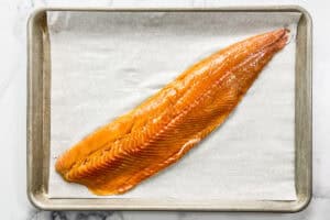 A trout fillet on a parchment lined rimmed baking sheet.