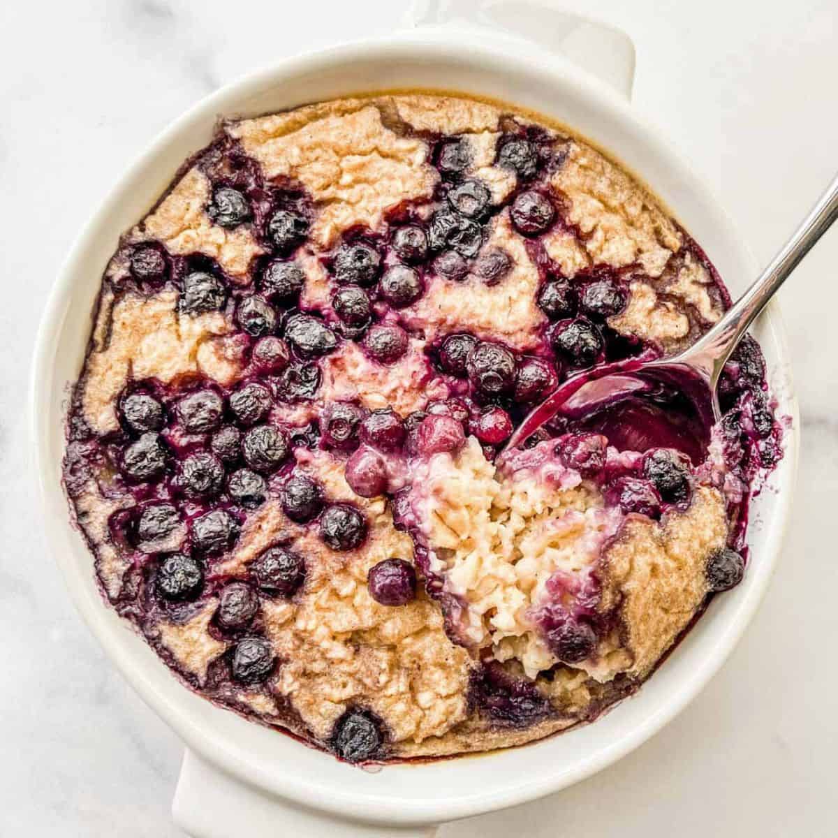 Blueberry baked oats in a white ramekin with a spoon.