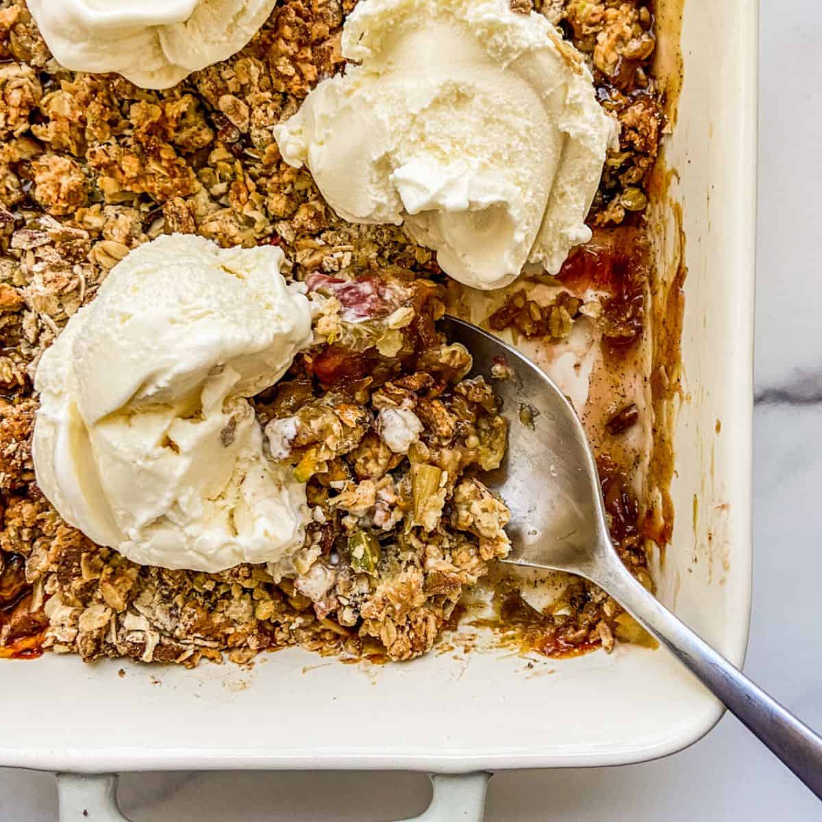 Rhubarb crisp in a baking dish topped with vanilla ice cream.