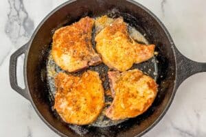 Four parmesan garlic crusted pork chops in a large cast iron pan.