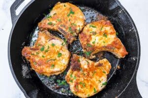 Four garlic parmesan pork chops in a large cast iron skillet.