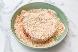 A pork chop being dredged in flour and parmesan.