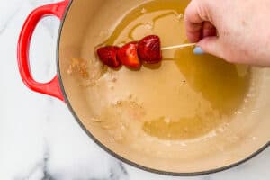 A skewer with strawberries being dipped into sugar.
