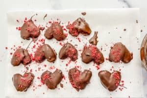 Chocolate date hearts topped with freeze dried raspberries drying on a pieces of parchment paper.