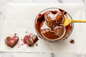 Heart shaped dates being dipped in melted chocolate.