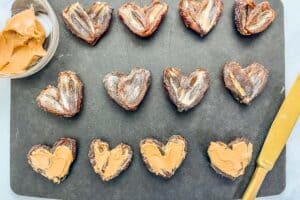 Halved dates pressed together in a heart shape being filled with peanut butter.
