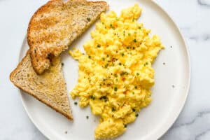 Cottage cheese eggs topped with chives on a white plate with a piece of toast.