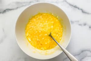 Eggs and cottage cheese whisked together in a white bowl with a silver fork.