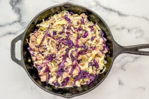 Cabbage added to ground pork in a cast iron skillet.