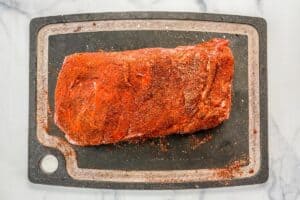 Pork shoulder with a spice rub on a black cutting board.