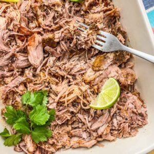 A fork picking up shredded carnitas from a pan.