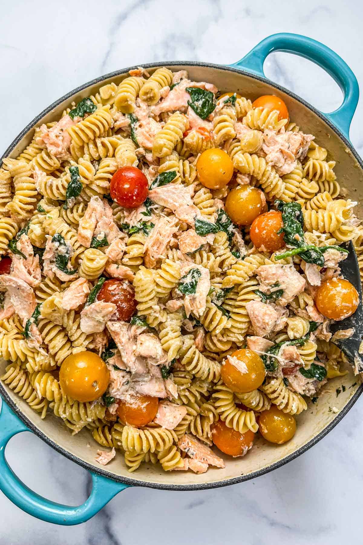 Salmon boursin pasta with tomatoes and spinach in a large teal pot.