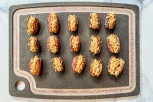 Dates filled with kataifi and pistachio on a black cutting board.