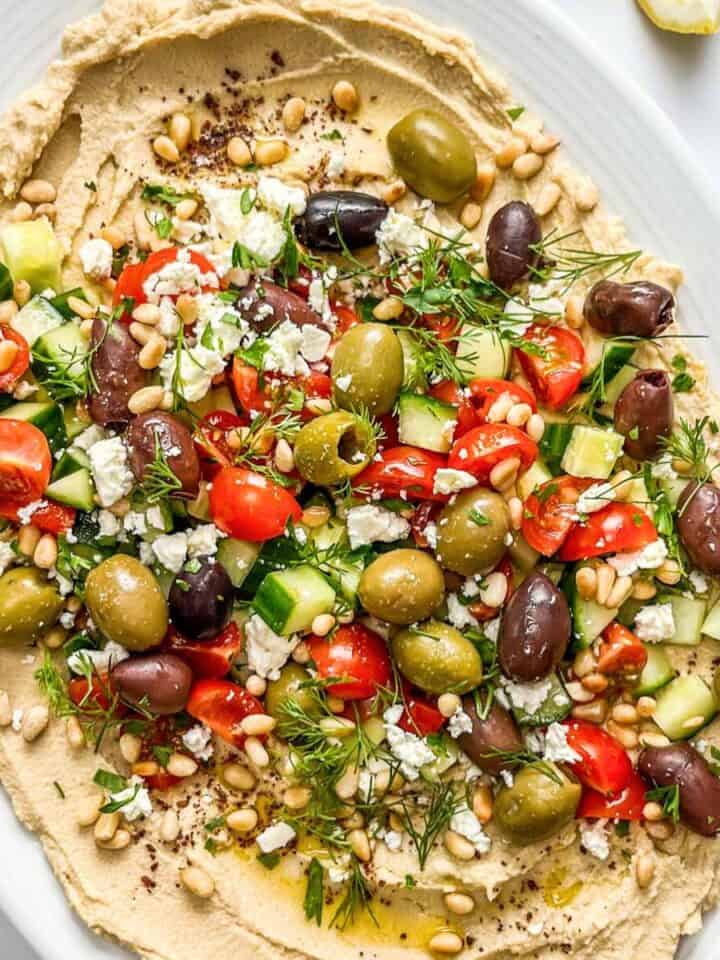 Hummus loaded with olives, cucumber, feta, pine nuts, dill, and olive oil.