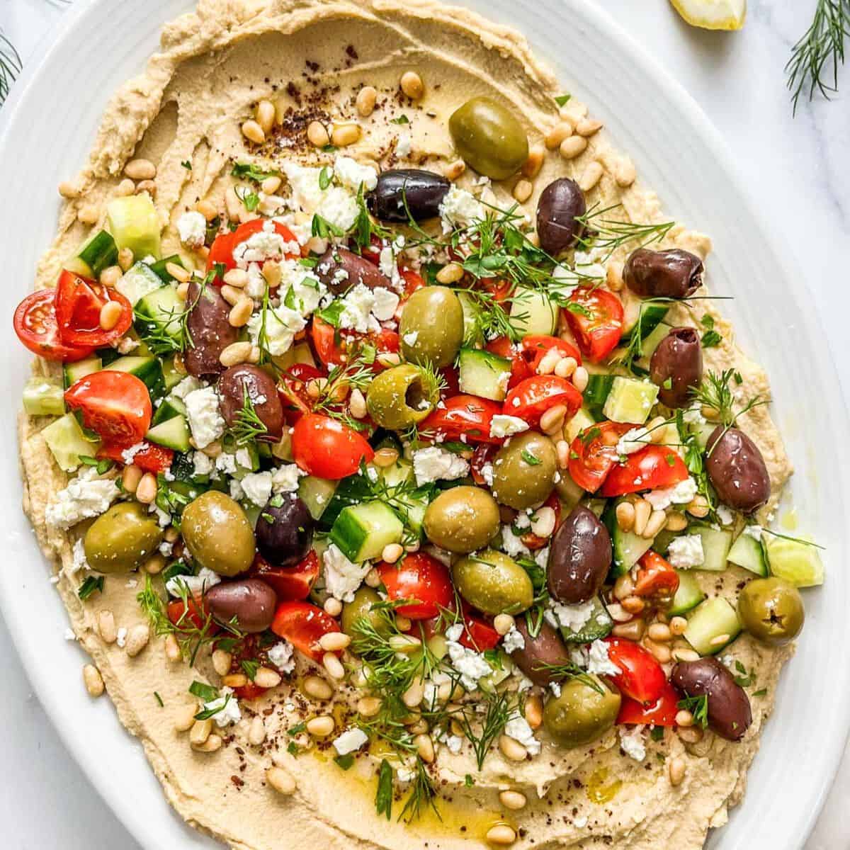 Hummus loaded with olives, cucumber, feta, pine nuts, dill, and olive oil.