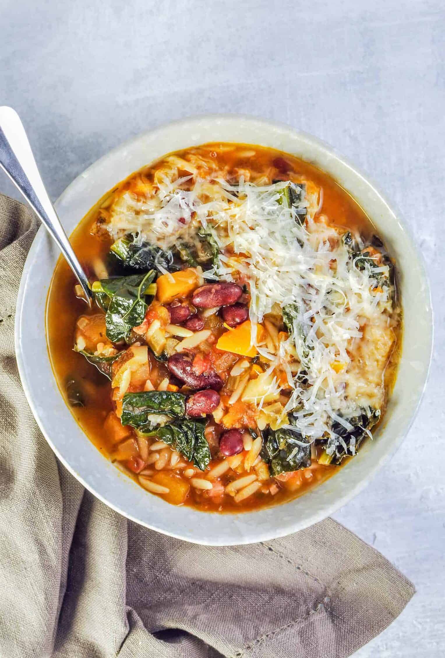 Pumpkin minestrone soup in a bowl next to a napkin.