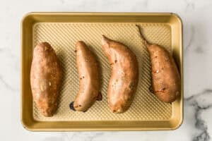 Four roasted sweet potatoes on a gold sheet pan.