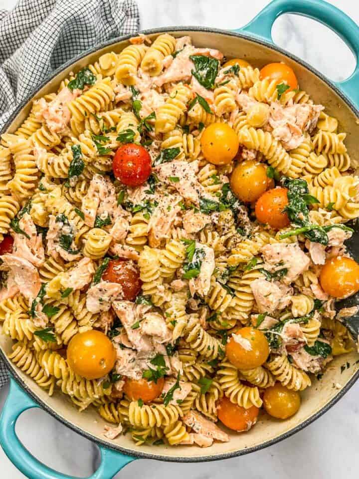 Salmon boursin pasta with cherry tomatoes in a skillet with a wooden spoon.