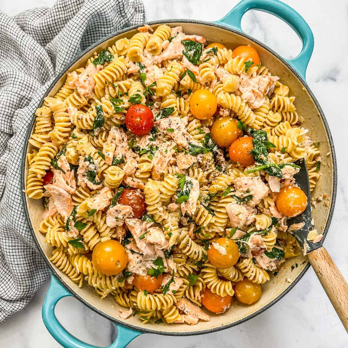 Salmon boursin pasta with cherry tomatoes in a skillet with a wooden spoon.