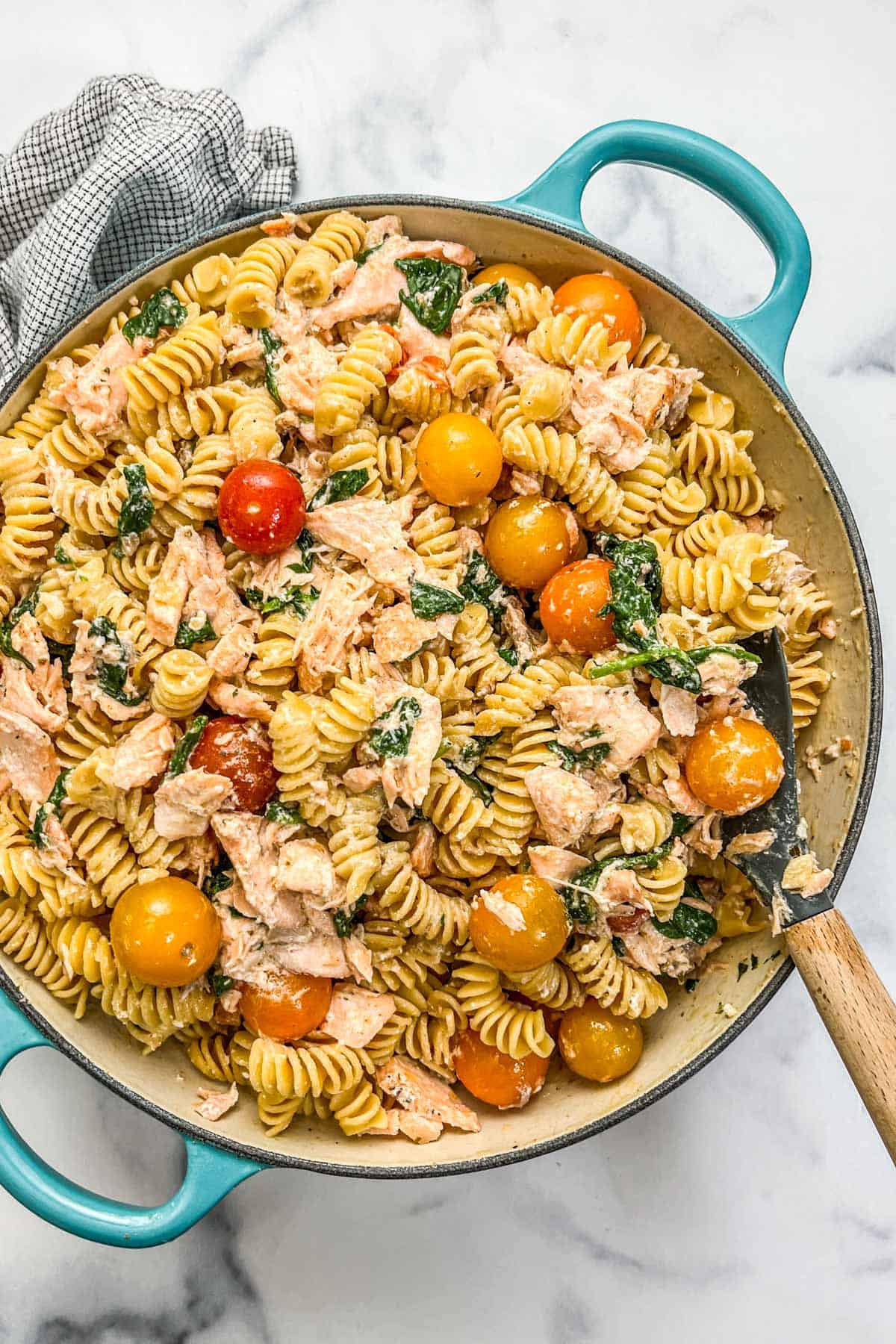 Boursin salmon pasta with tomatoes in a large pot with a wooden spoon.