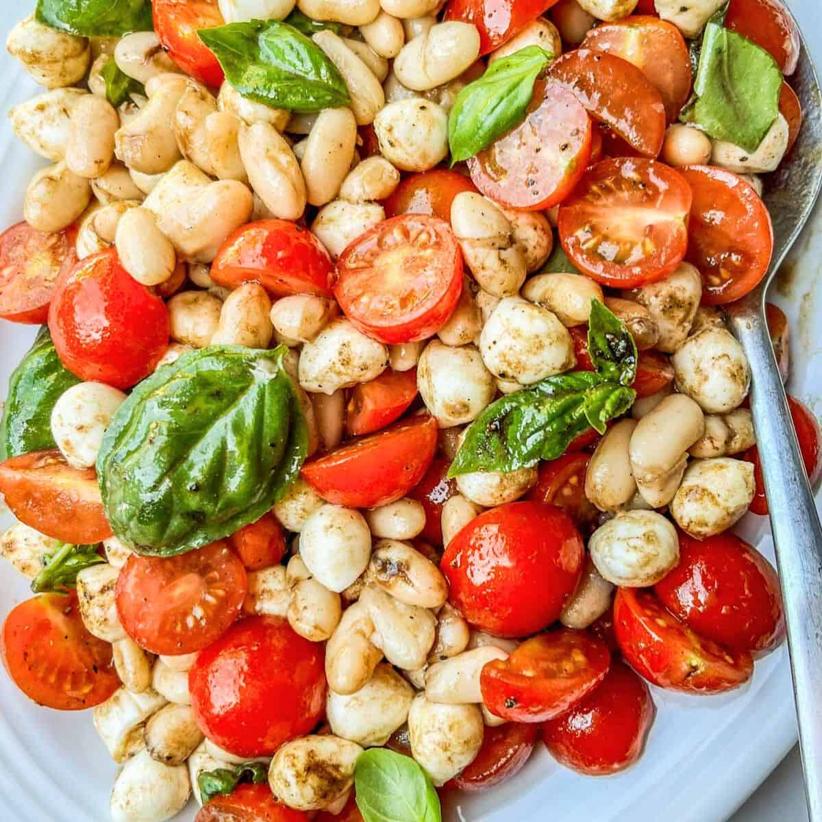 White bean caprese salad on a white platter with a spoon.