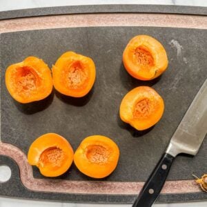 Halved apricots on a black cutting board.