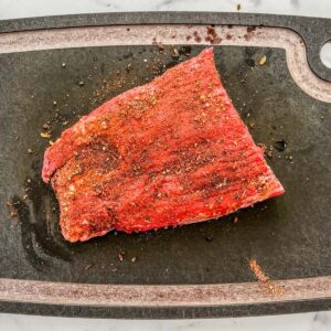 Flank steak covered in spices on a cutting board.