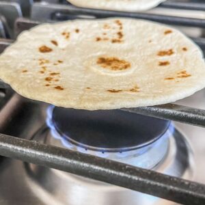 A tortilla being heated on a gas range.