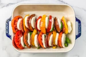 Sliced of heirloom tomatoes, salami, mozzarella, and basil in a baking dish.