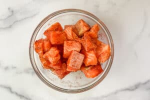 Salmon chunks tossed with spices in a glass bowl.