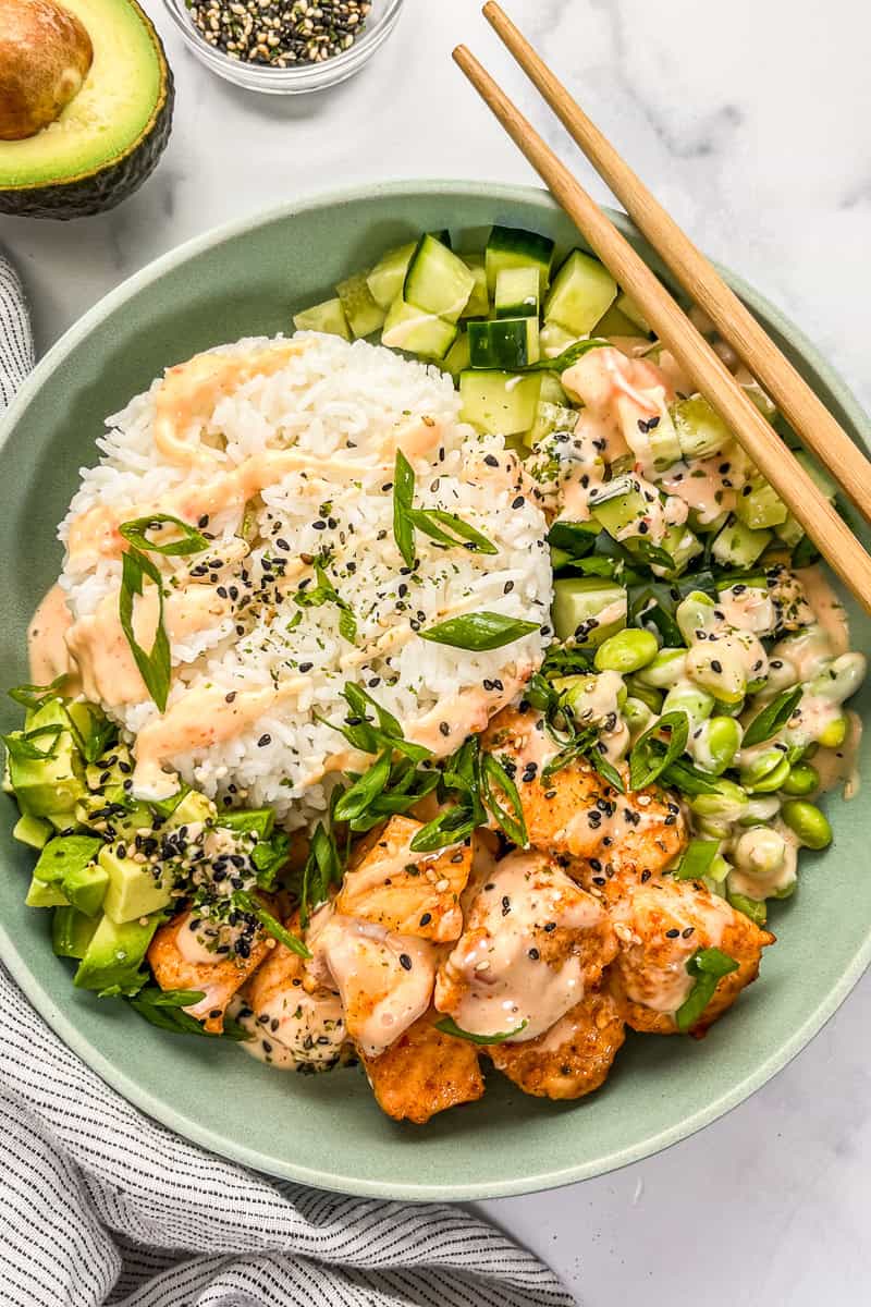 Bang bang salmon and rice bowl with veggies with chopsticks.